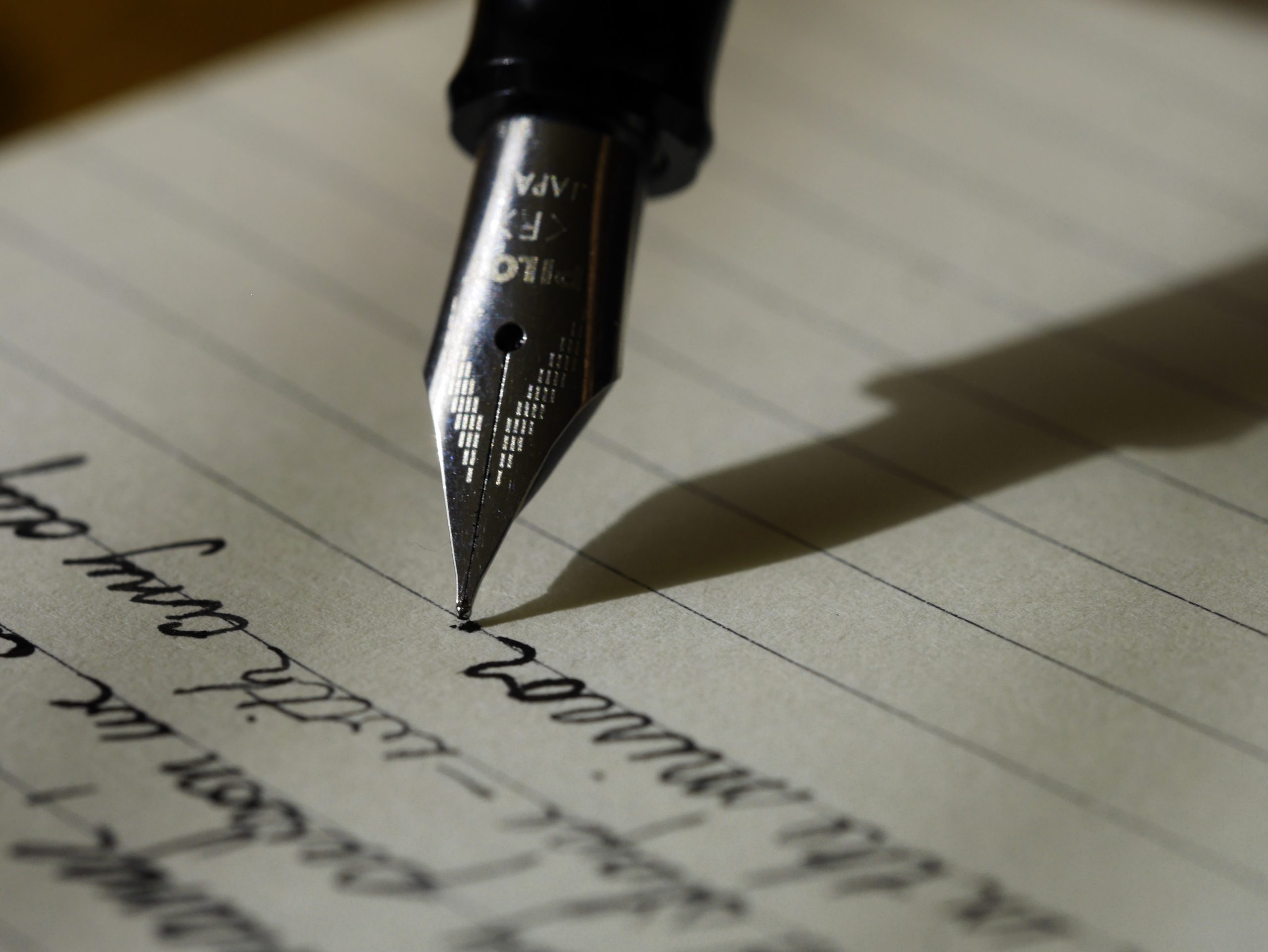 Close up image of a fountain pen writing in cursive on notebook paper.