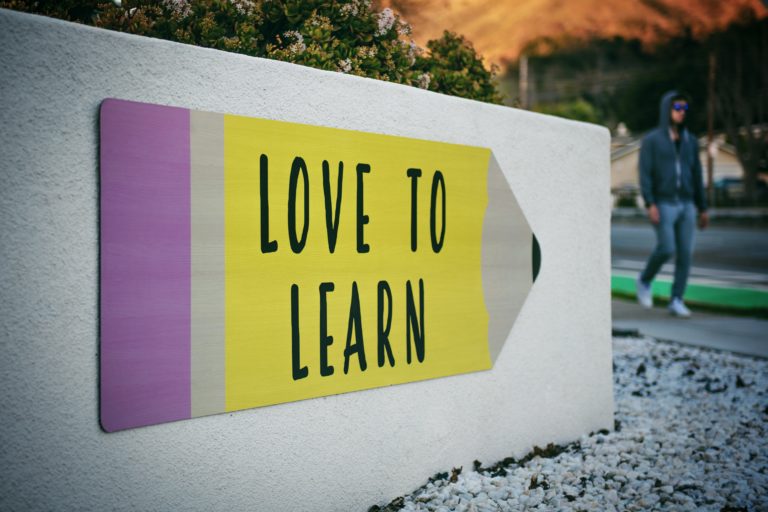 A large white sign with a cartoon drawing of a huge, short, thick pencil. The words on the pencil read love to learn in black lettering.